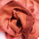 Cusubamba baby alpaca wool blanket – a plush, reddish-orange fabric is loosely and artfully gathered, creating soft folds. The texture appears smooth and fuzzy, suggesting warmth, with the fabric resting against a plain background