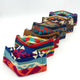Colorful fabric face masks with geometric patterns are arranged in a line, showcasing earth tones and vibrant blues and oranges against a plain white background.
