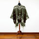 Clint Eastwood alpaca wool poncho – a dark green, patterned poncho drapes over a mannequin with a wooden stand, set against a plain white wall and wooden floor