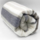 Yacoubina baby alpaca wool blanket – a rolled multicolored blanket with horizontal white, beige, gray, and brown stripes rests on a plain white background