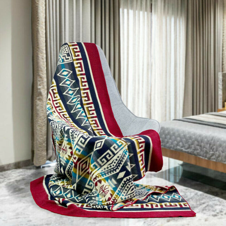 A colorful, patterned blanket drapes over a sleek, modern chair in a bedroom. The room features floor-length curtains, a bed with a quilt, and a marble floor.