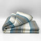 Chuquipogyo baby alpaca wool blanket – a neatly folded blanket displaying stripes in blue, gray, and white rests on a plain surface, set against a soft gradient background