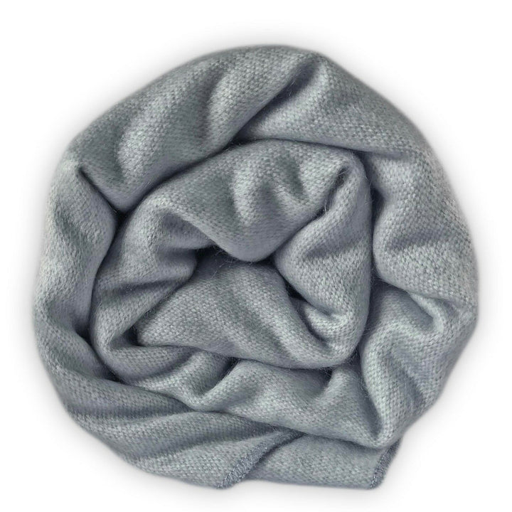 Suncamal baby alpaca wool blanket – a soft, light grey blanket is rolled into a spiral pattern, creating a textured, cozy appearance against a plain white background