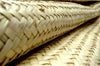 A tightly woven straw mat, curled slightly at the edges, lies on a flat surface. The texture is prominent, showcasing intricate crafting patterns in a well-lit environment.