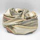 Ducur baby alpaca wool blanket – a soft, multi-colored blanket with pastel shades is artistically draped in a loose coil against a plain white background, displaying its subtle striped pattern