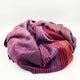 Pallatanga baby alpaca wool blanket – a crumpled, multicolored blanket with shades of purple, red, and orange lies on a white surface, showcasing its soft texture and striped pattern