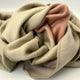 Tilivi baby alpaca wool blanket – a soft, beige fabric with hints of pink is crumpled and layered. It rests on a plain surface, highlighting its texture and stitching details