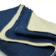 A folded blue and beige blanket with stitched edges lies on a white surface, showcasing its dual-tone fabric.