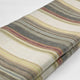 Ducur baby alpaca wool blanket – a folded multi-colored fabric with horizontal, wavy stripes lies on a white surface. The stripes blend earthy tones, including gray, olive, beige, and subtle hints of red and yellow