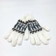 White knitted gloves lie together on a flat, plain surface, featuring dark gray and brown Nordic patterns around the wrists, creating a cozy winter theme.