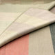 Tilivi baby alpaca wool blanket – a folded, soft-textured blanket with pastel color blocks (pink, cream, green) lies over another layer, creating a cozy, layered appearance. No text is present