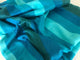 Cajabamba alpaca wool blanket – a piece of fabric with horizontal blue and turquoise stripes lies crumpled, showcasing its soft texture. The fabric is unevenly draped, creating folds and shadows