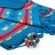 A colorful woven fabric with geometric patterns and fringed edges lies atop a folded blue cloth. Nearby, a bracelet of multicolored stones sits on the fabric.