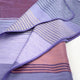 Ochoa baby alpaca wool blanket – a soft, folded blanket displays a pattern of purple and lavender stripes, overlapping gently on a smooth, neutral surface, creating a cozy and inviting texture