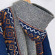 A patterned knitted sweater featuring geometric designs in blue, brown, and white. The sweater is folded over a wooden hanger against a plain white background.