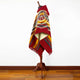 Guismi alpaca wool hooded poncho – a mannequin displays a vibrant red and multicolored patterned poncho, standing upright in a brightly lit room with wooden flooring and white walls