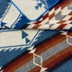 A folded textile displays geometric patterns in blue, white, and brown shades with a blue-bordered edge, underscoring a bold, southwestern-inspired design theme.