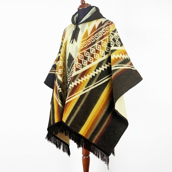 A poncho is displayed on a mannequin, featuring geometric patterns with earth tones and fringe at the hem. The background is plain white, highlighting the garment's intricate design.