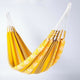 A yellow and orange striped hammock, hanging suspended. The hammock is open and empty, set against a plain white background.