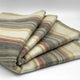 Ducur baby alpaca wool blanket – a folded wool blanket displays soft, multicolored horizontal stripes with shades of beige, gray, green, and pink, lying atop a plain white surface