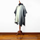 Zuleta llama wool hooded poncho – a gray poncho with a ribbed texture is displayed on a wooden mannequin. It stands against a plain white background on a polished hardwood floor