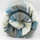 Chuquipogyo baby alpaca wool blanket – a rolled-up, multicolored knitted blanket with stripes of blue, gray, and white is positioned against a plain, light background