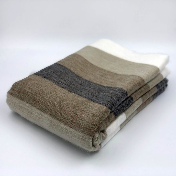 Mogato baby alpaca wool blanket – a folded blanket featuring broad horizontal stripes in muted earth tones rests on a smooth, white surface, with no additional objects or text present in the minimalist setting
