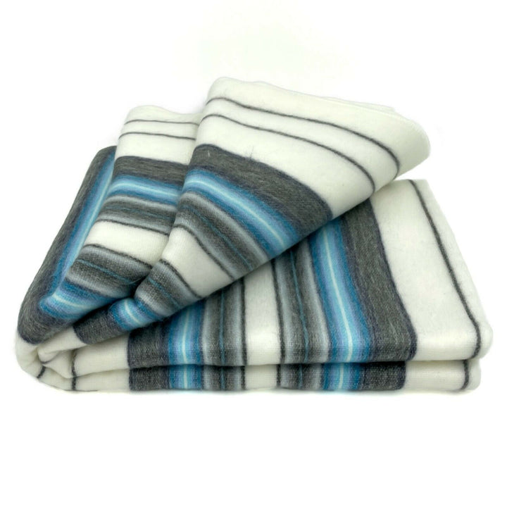 Teinza baby alpaca wool blanket – a folded blanket displays horizontal stripes in varying shades of white, gray, and blue, set against a plain white background