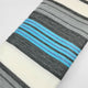Aychapicho baby alpaca wool blanket – a folded fabric features horizontal stripes in shades of gray, white, and blue, lying on a plain white surface, showcasing a repeating pattern. No text is present