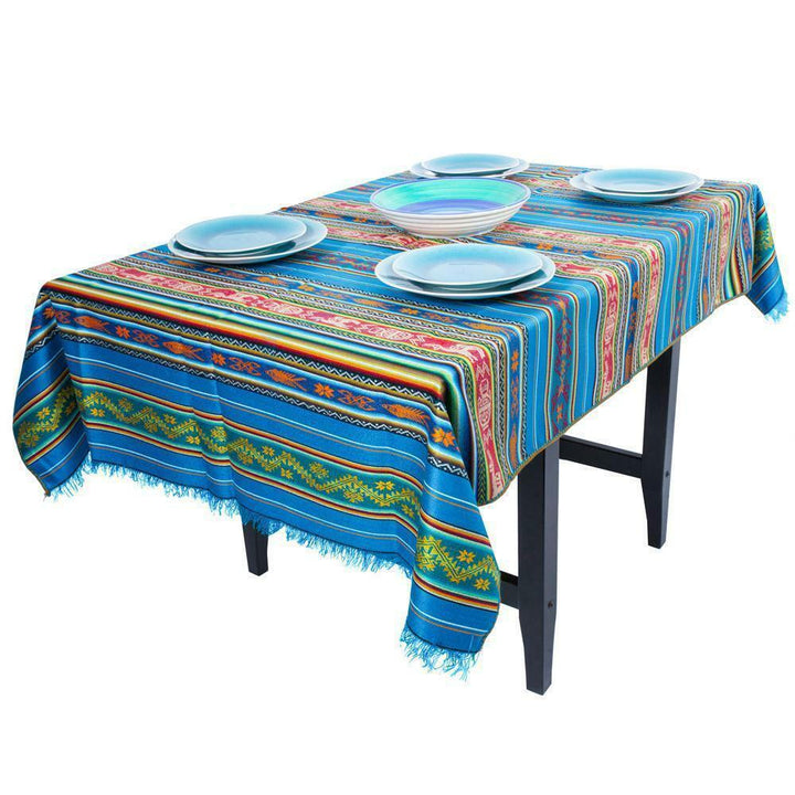 A colorful woven tablecloth with intricate patterns covers a rectangular table, adorned with five blue and white ceramic plates, creating a vibrant dining setting.