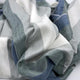 Poguios baby alpaca wool blanket – fabric with broad stripes in shades of green, gray, and white, loosely draped. The texture appears soft and woven, suggesting a cozy or decorative textile