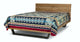 A wooden bed frame supports a bed covered with a colorful, geometric-patterned blanket. The design features diamonds and intricate shapes, set against a minimal, white background.