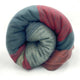 Atacazo baby alpaca wool blanket – a rolled up, multi-colored blanket featuring shades of green, red, and orange is displayed against a plain white background. The textures vary, including smooth and fuzzy sections