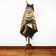 A poncho with geometric patterns and earthy tones is draped on a mannequin stand in a room with wooden flooring and a plain white wall background.