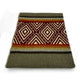A folded blanket displays geometric diamond patterns in maroon, cream, and orange, bordered by stripes on a gray background. The setting is a plain white surface.