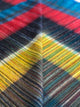 Alpaca wool queen blanket – a colorful, textured fabric displays intersecting stripes of red, blue, yellow, and green, folded slightly at an angle, suggesting a close-up view of a textile pattern