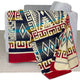 A patterned blanket drapes over a gray sofa, featuring geometric designs in red, blue, and gold tones. The setting includes a light-colored carpet, creating a cozy atmosphere.