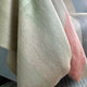 Tilivi baby alpaca wool blanket – fabric swatches drape over a surface, showcasing a gradient of muted tones including beige, pink, and gray, adding a soft texture to the surroundings