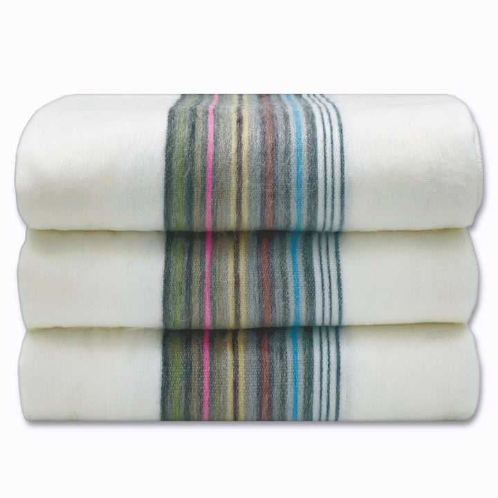 Sigchos baby alpaca wool blanket – three folded white blanket with colorful vertical stripes stacked neatly in a plain, well-lit environment