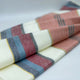 Rucu baby alpaca wool blanket – a folded piece of fabric lies on a surface, featuring horizontal stripes in red, blue, gray, and white. The fabric appears soft and is arranged neatly