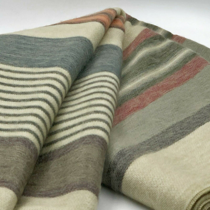 Suropata baby alpaca wool blanket – a folded woolen blanket displays stripes in muted colors, like gray, beige, and red, resting against a plain, light background