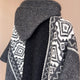 Gray knitted sweater with an intricate black and white geometric pattern, draped to show its large collar, against a plain beige background.