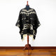 Clint Eastwood alpaca wool poncho – mannequin wearing a black poncho with white geometric patterns stands in a room with wooden flooring and a plain white wall