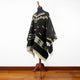Clint Eastwood alpaca wool poncho – a black and white poncho with geometric patterns is displayed on a mannequin. It stands on a wooden floor against a white background