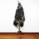 Clint Eastwood alpaca wool poncho – a black poncho with white geometric patterns drapes over a wooden mannequin stand, set against a plain white wall and wooden floor