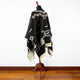 Clint Eastwood alpaca wool poncho – mannequin displaying a black and white patterned poncho with tassels draped over it, set against a white wall and wooden floor