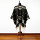 Clint Eastwood alpaca wool poncho – a black poncho with white geometric patterns is displayed on a wooden mannequin stand, set against a white wall and wooden floor