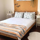 Tumbunuma baby alpaca wool blanket – bed with patterned pillows and striped blanket rests in a cozy bedroom. Good night text is on the warm-toned wall. Nearby, there are side tables and a small blanket