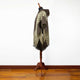 A brown and beige patterned poncho with fringe edges is displayed on a wooden mannequin stand, set against a plain white background with a wooden floor.