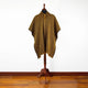 A black and yellow striped poncho is displayed on a wooden stand against a white wall, with a wooden floor beneath.
